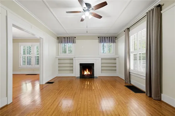a view of a room with wooden floor a fireplace a ceiling fan and windows