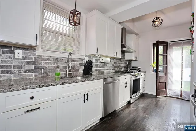 a kitchen with a sink dishwasher a stove and white cabinets with wooden floor