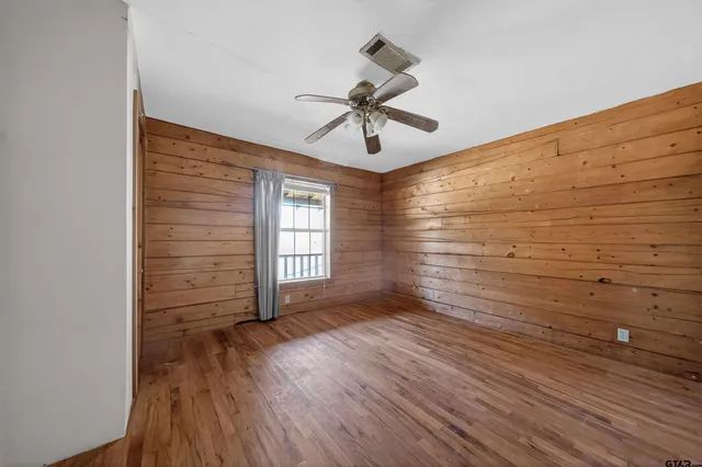 a view of empty room with wooden floor and fan