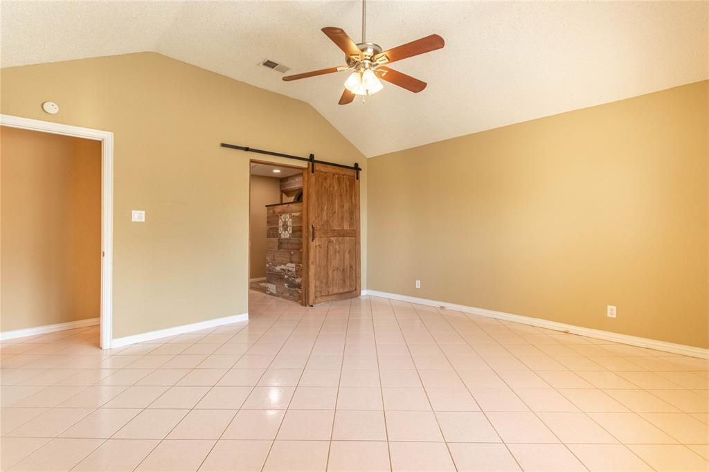 308 Sanders Road Denton, TX 76210 - Photo 2 of 31 Vaulted ceiling, ceiling fan with light fixture, light-toned floor tile, wood barn door, and stone accent wall