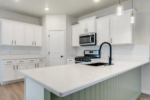 a kitchen with stainless steel appliances a stove a sink a refrigerator white cabinets and wooden floor