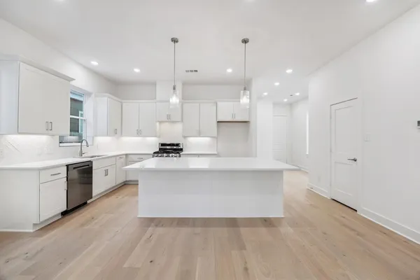 a large white kitchen with a stove a sink dishwasher and a refrigerator with wooden floor