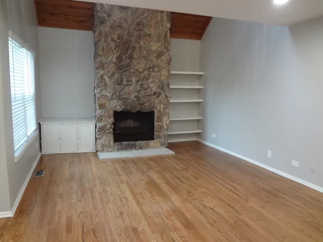 a view of an empty room with wooden floor fireplace and a window