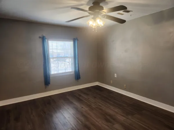 an empty room with wooden floor fan and windows