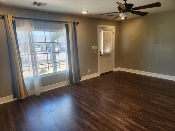 an empty room with wooden floor a ceiling fan and windows