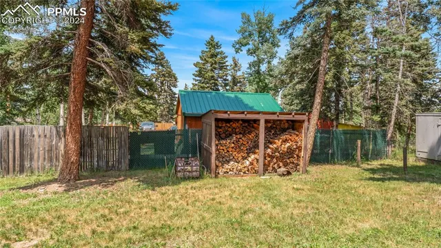 a view of wooden house with large trees and wooden fence