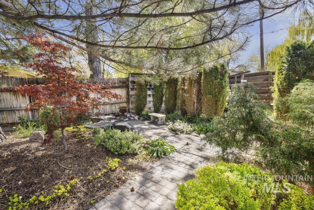 2018 Rancho Vista Drive Twin Falls, ID 83301 - Photo 46 of 50 Landscaped backyard featuring a paver patio, a variety of mature trees and shrubs, a defined planting bed with mulch, a stone bench, and a wood privacy fence