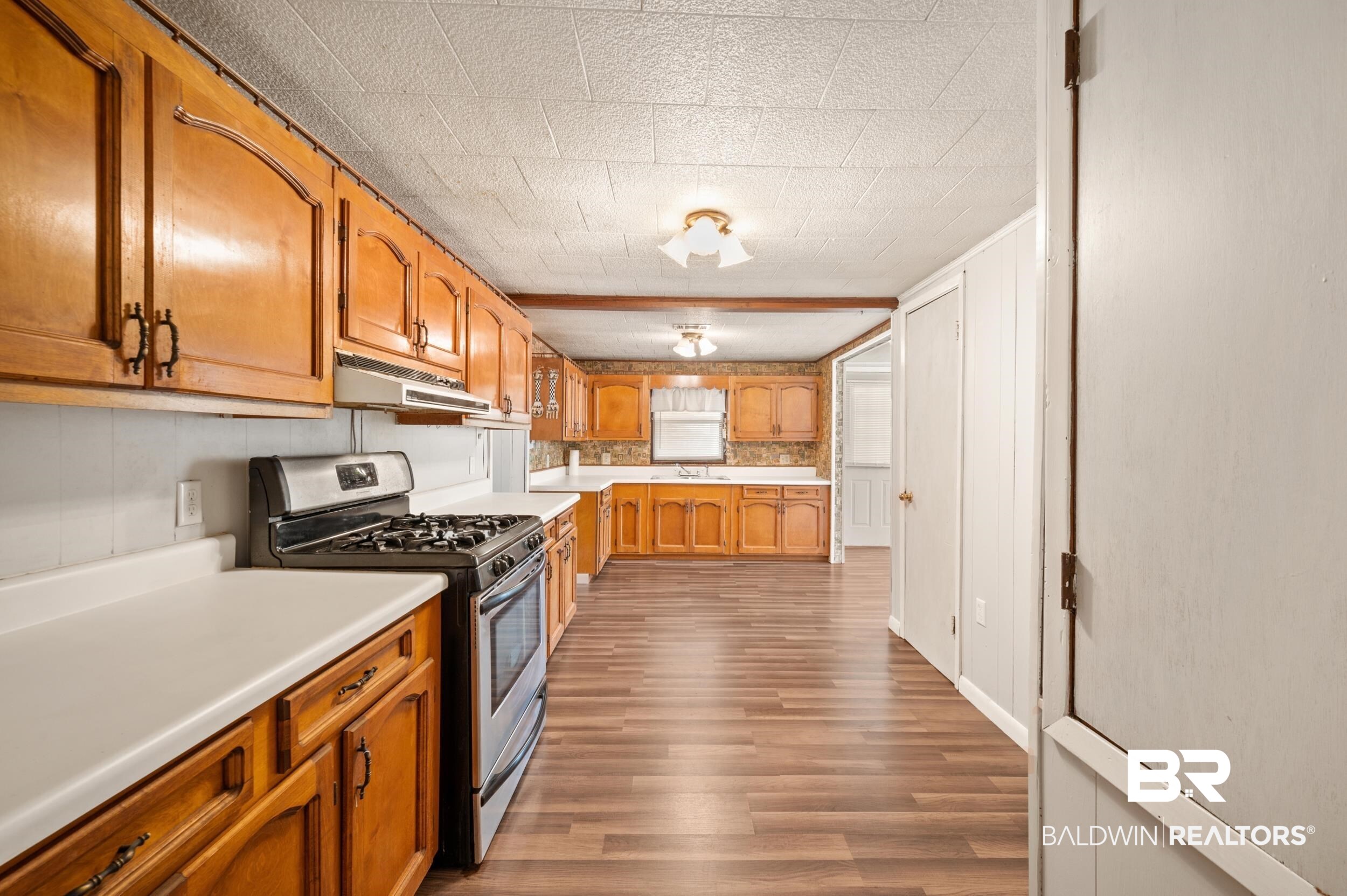 57623 Mary Hadley Road Perdido, AL 36562 - Photo 6 of 34 Kitchen featuring gas stove, brown cabinets, light countertops, dark wood finished floors, and under cabinet range hood