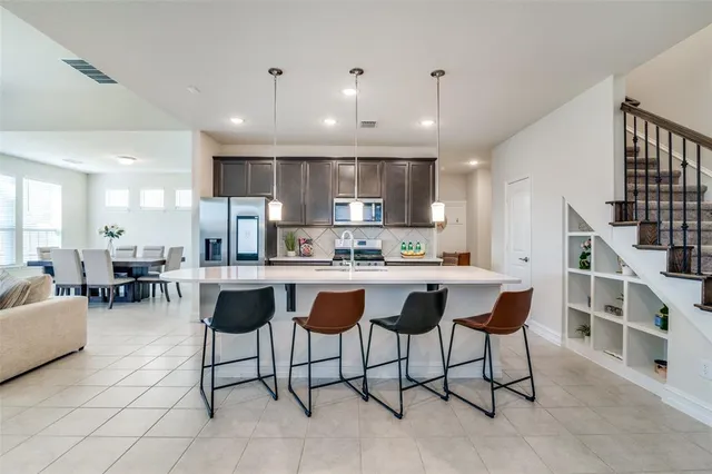 a kitchen with stainless steel appliances kitchen island granite countertop a dining table chairs refrigerator and cabinets