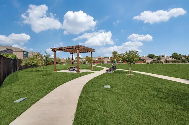 a view of a fountain in front of a big yard with plants and large trees