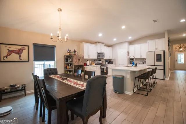 a view of a dining room and livingroom with furniture wooden floor a rug a flat screen tv a painting and a chandelier