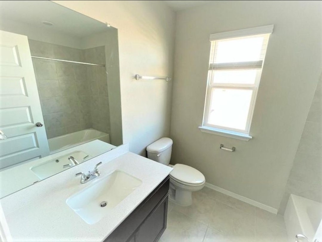 2771 Winding Creek Road Kyle, TX 78640 - Photo 17 of 24 A well-lit primary bathroom features a generous vanity, a clean white toilet, and a tiled tub.