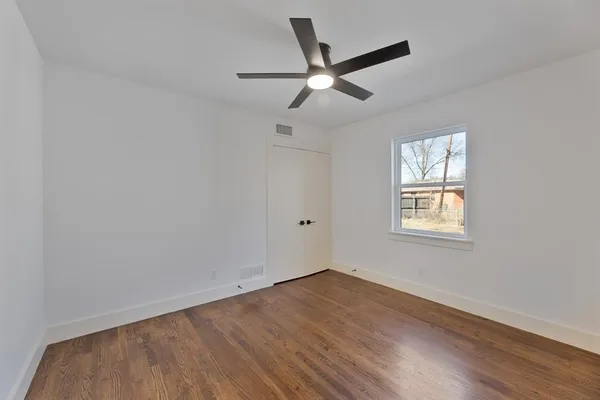 an empty room with wooden floor ceiling fan and windows