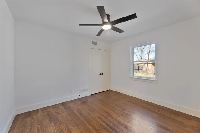 an empty room with wooden floor ceiling fan and windows