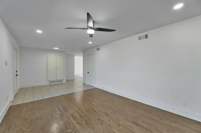 an empty room with wooden floor ceiling fan and windows