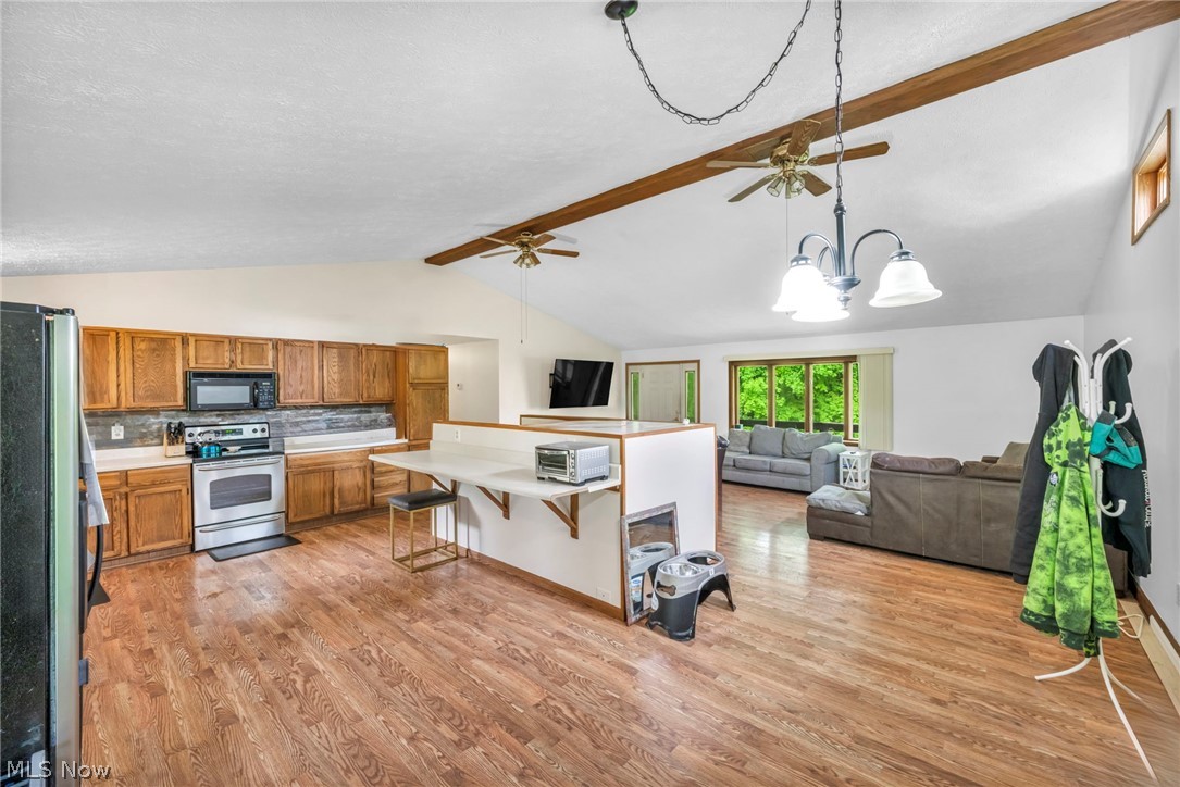 4560 Arrow Road Northwest Carrollton, OH 44615 - Photo 7 of 41 Kitchen featuring ceiling fan with notable chandelier, hanging light fixtures, range, light wood-type flooring, and lofted ceiling with beams