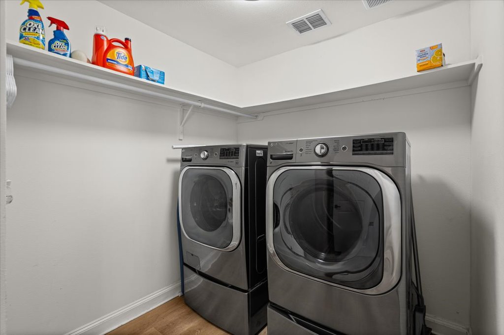 1201 Garden Street, Unit A Austin, TX 78702 - Photo 13 of 30 Dedicated laundry area featuring dual front-loading appliances, upper wall shelving, wood-finish flooring, and white baseboards