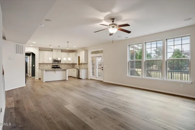 a view of an empty room with wooden floor and a kitchen