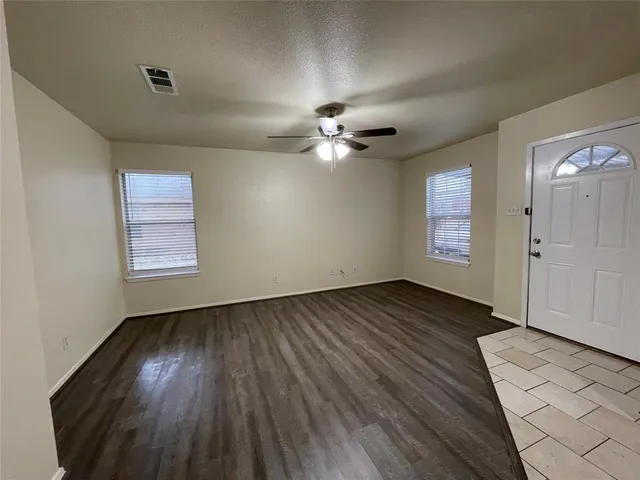 an empty room with wooden floor chandelier fan and windows