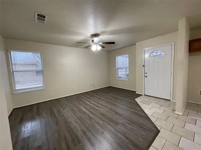 an empty room with wooden floor chandelier fan and windows