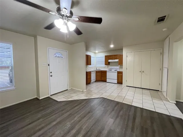 an empty room with wooden floor kitchen view and a window