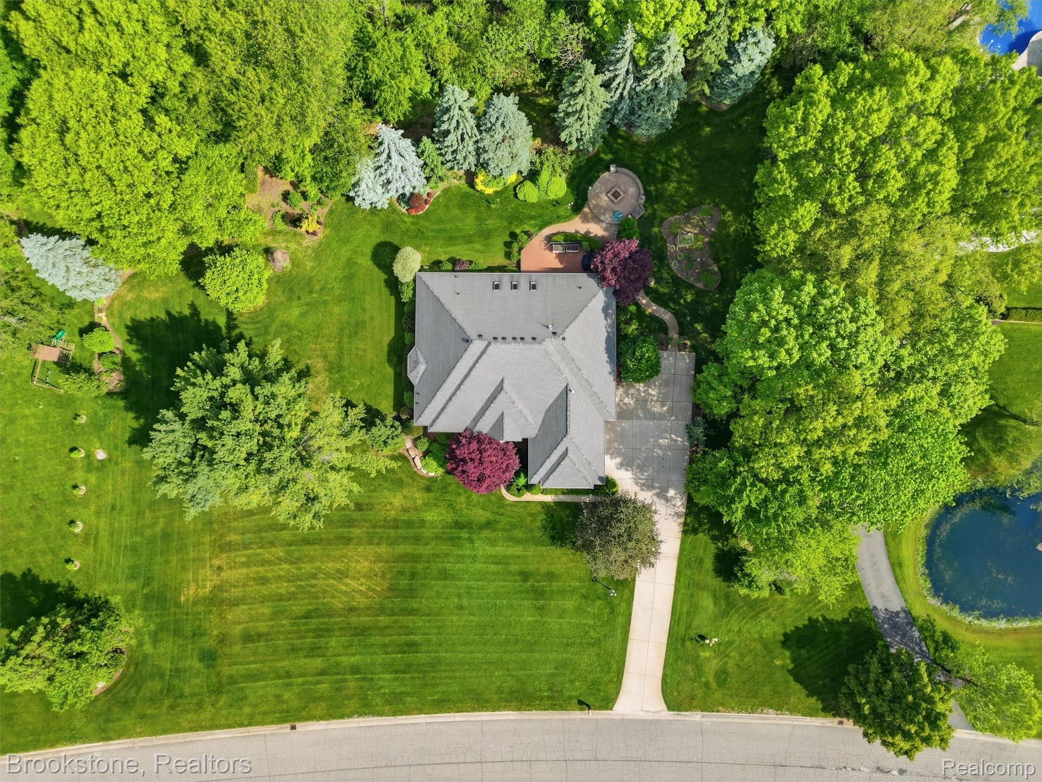9523 Quail Ridge Run Brighton, MI 48114 - Photo 6 of 50 Expansive property featuring a multi-gabled roofline, lush green lawn, mature trees, a paved driveway, and a circular paved patio with a fire pit