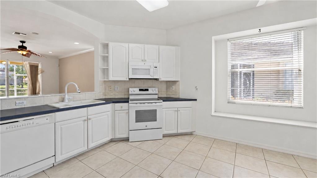 7737 Haverhill Court Naples, FL 34104 - Photo 11 of 37 Kitchen featuring white cabinetry, integrated appliances, dark countertops, tiled flooring, and a large window with a deep sill
