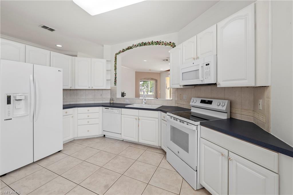 7737 Haverhill Court Naples, FL 34104 - Photo 12 of 37 Spacious kitchen featuring white cabinetry, dark countertops, a built-in microwave, a full-size refrigerator, and tile flooring