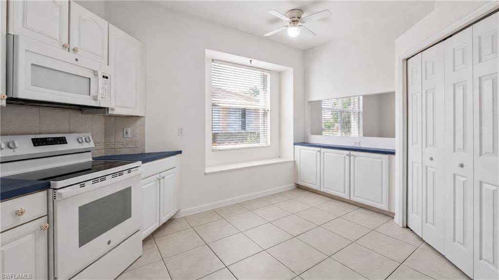 7737 Haverhill Court Naples, FL 34104 - Photo 13 of 37 Kitchen area featuring white cabinetry, a built-in microwave, a white electric range, blue countertops, and neutral-toned tile flooring