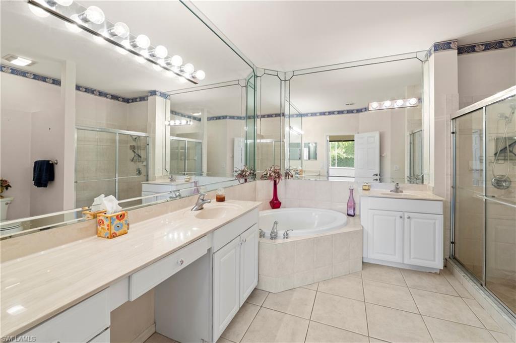 7737 Haverhill Court Naples, FL 34104 - Photo 22 of 37 Dual vanity bathroom featuring a built-in jetted tub, separate glass-enclosed shower, extensive mirror work, and square floor tiles