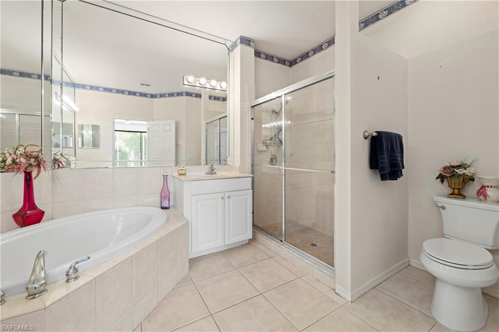 7737 Haverhill Court Naples, FL 34104 - Photo 23 of 37 Tiled bathroom featuring a built-in tub, separate shower with glass enclosure, white vanity, and a large wall-mounted mirror