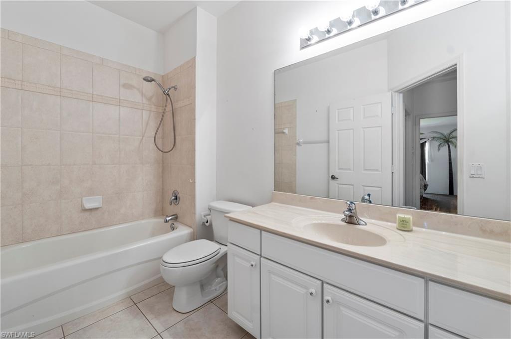 7737 Haverhill Court Naples, FL 34104 - Photo 24 of 37 Bathroom featuring a full-sized bathtub with tiled surround, a white toilet, and a vanity with a light-toned countertop and integrated sink