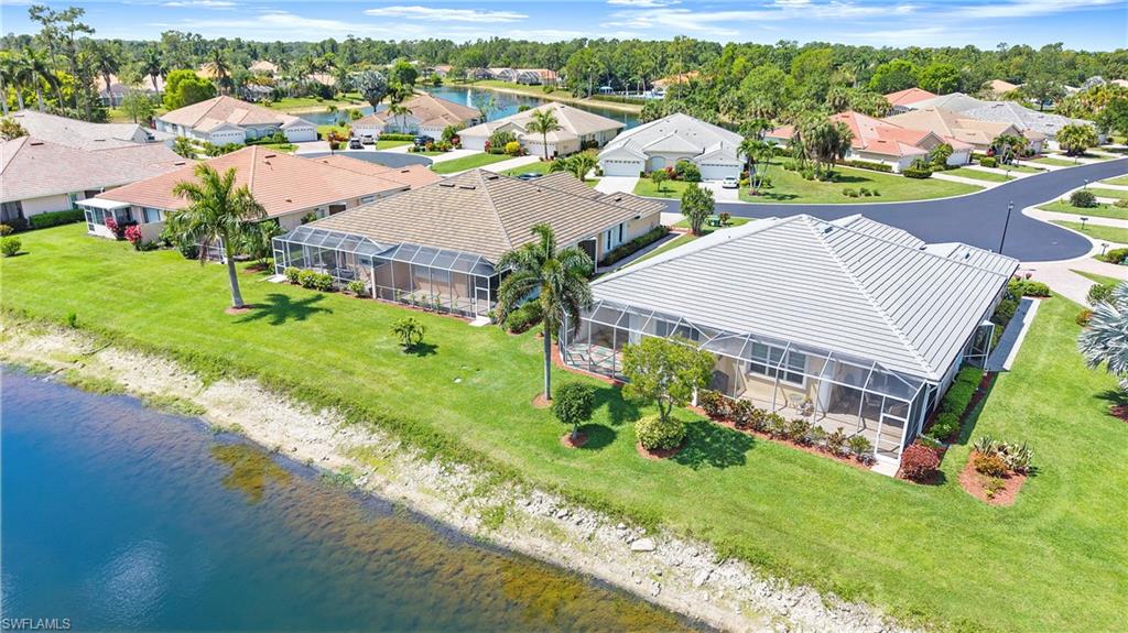 7737 Haverhill Court Naples, FL 34104 - Photo 33 of 37 Waterfront property featuring a screened lanai and mature landscaping, with a white tile roof and direct access to a paved street