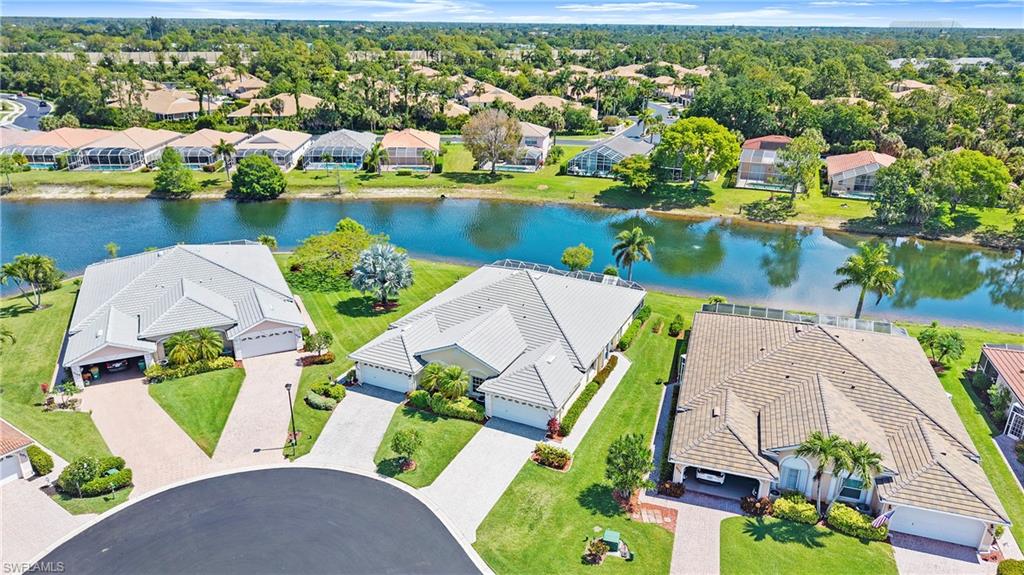 7737 Haverhill Court Naples, FL 34104 - Photo 36 of 37 Waterfront property featuring a tile roof, mature palm trees, manicured lawns, and a paved driveway leading to an attached garage