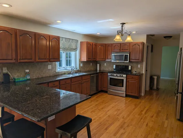 a kitchen with stainless steel appliances a sink a stove a microwave a refrigerator cabinets and wooden floor