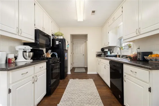 a kitchen with stainless steel appliances granite countertop a refrigerator a sink dishwasher and white cabinets with wooden floor