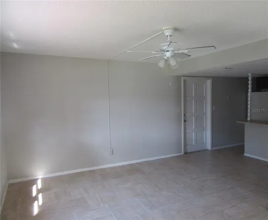 an empty room with chandelier fan and kitchen view