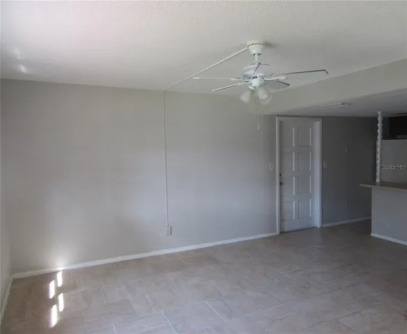 an empty room with chandelier fan and kitchen view