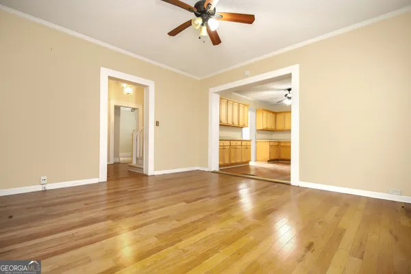 a view of an empty room with wooden floor and a ceiling fan