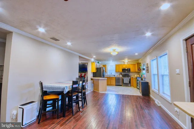 a living room with stainless steel appliances lots of furniture and wooden floors