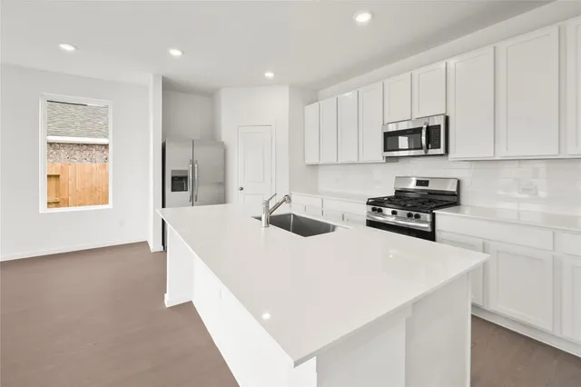 a kitchen with stainless steel appliances a sink a stove a microwave a refrigerator a white cabinets and wooden floor