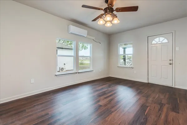 an empty room with wooden floor chandelier fan and windows