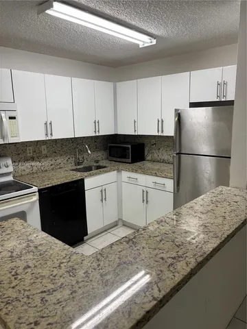 a kitchen with granite countertop a refrigerator sink and cabinets