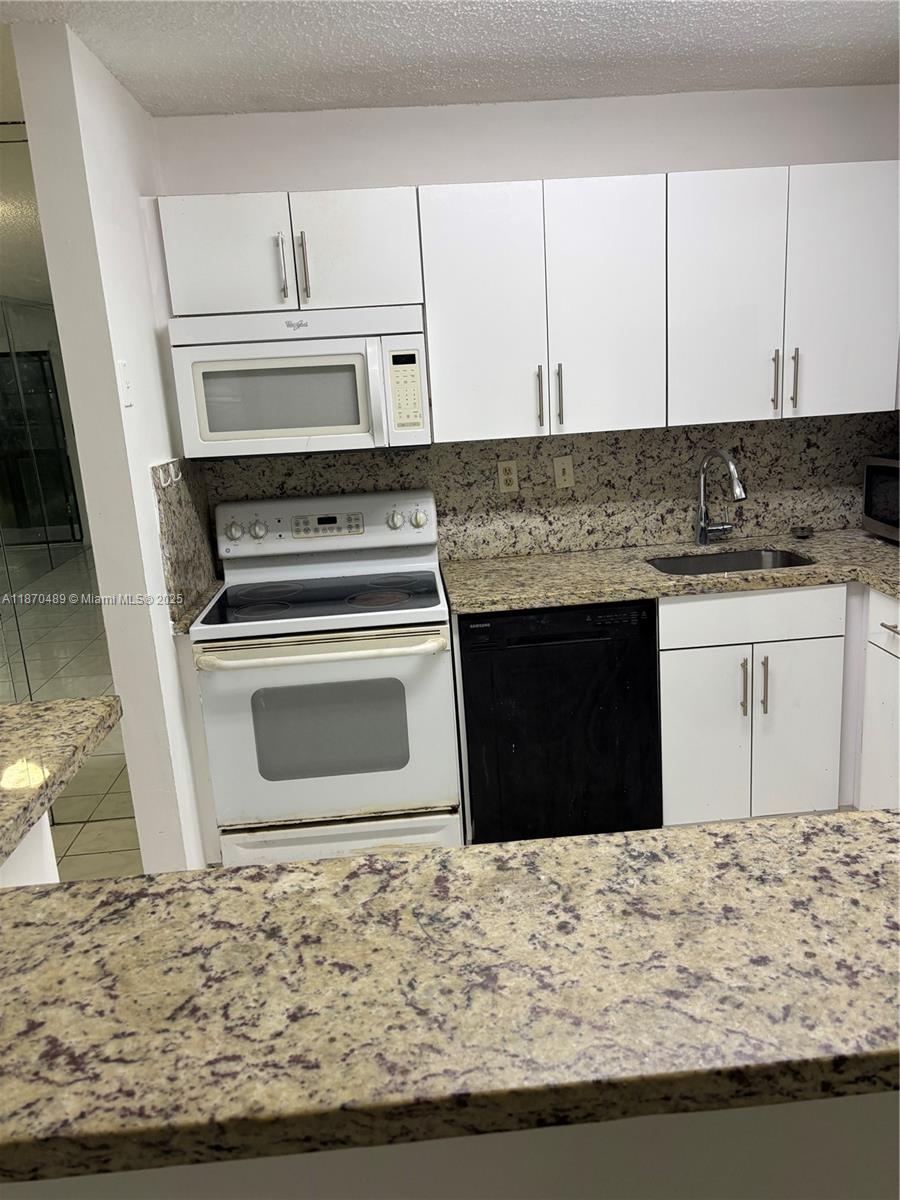 911 Northeast 199th Street, Unit 10414 Miami, FL 33179 - Photo 4 of 18 a kitchen with granite countertop a stove a sink and a microwave