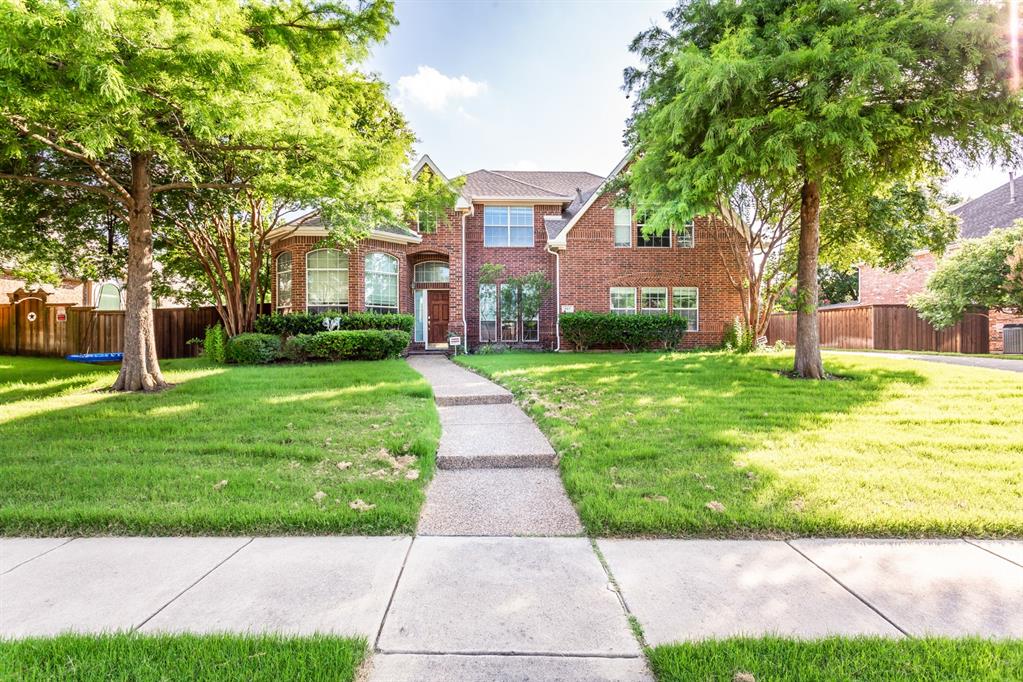 a view of a brick house with a big yard plants and large trees