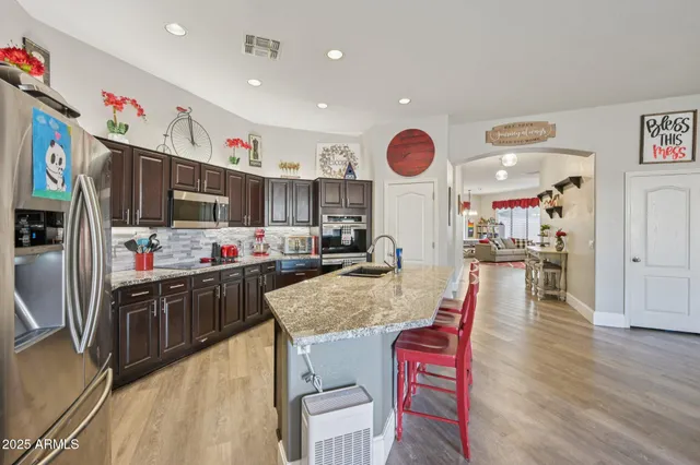 a kitchen with stainless steel appliances granite countertop a refrigerator a stove top oven and a dining table with wooden floor