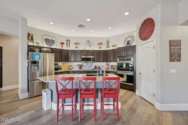 a kitchen with stainless steel appliances granite countertop a dining table chairs refrigerator and sink