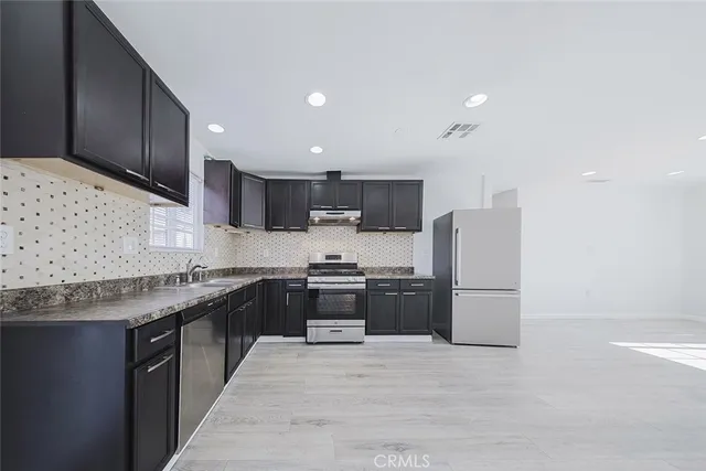 an empty room with wooden floor kitchen view and windows