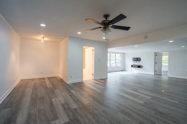 an empty room with wooden floor fan and windows