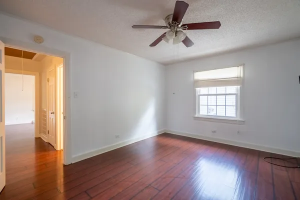 an empty room with wooden floor fan and windows
